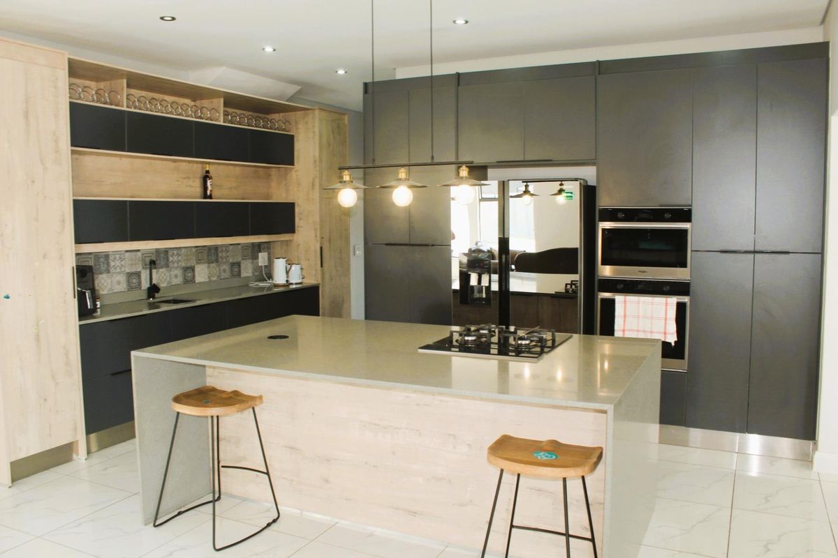 Modern kitchen featuring a large central island with a gas hob, integrated appliances, sleek dark cabinetry, and high-quality stone countertops.