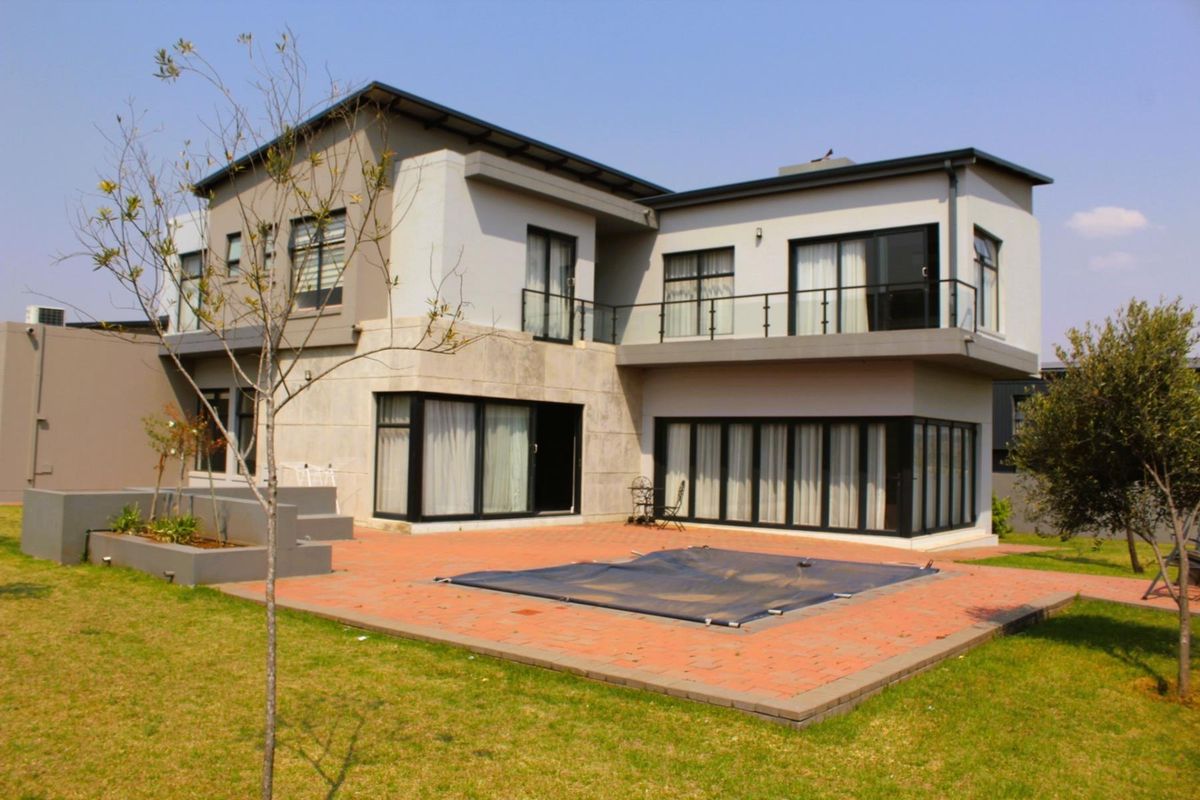 Rear view of a modern two-story house featuring a paved patio, swimming pool, and an upper-level balcony with glass balustrades.