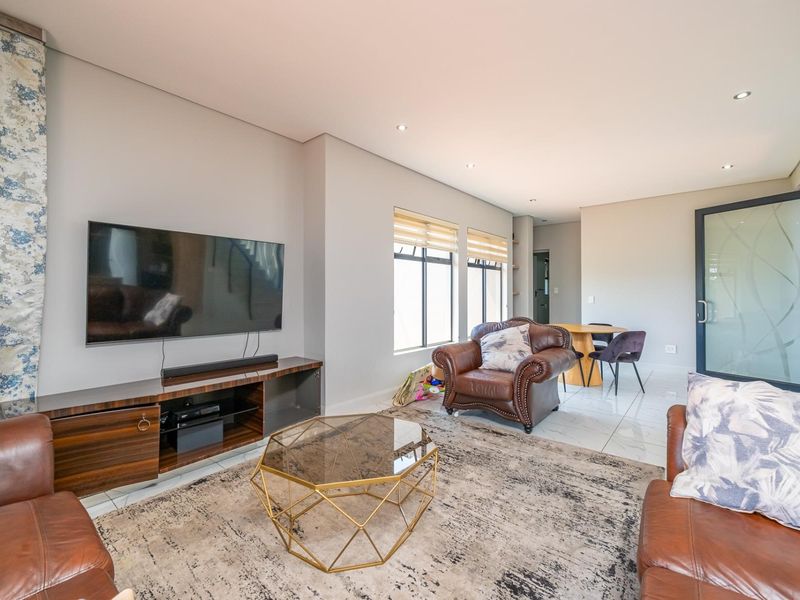 A bright and modern living room featuring tiled flooring, recessed downlights, and a glass panel door, offering a clean and contemporary living space.