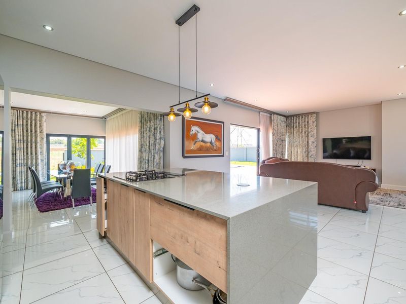 Spacious open-plan living area featuring a modern kitchen island with a gas hob, stone countertops, and seamless flow to the dining and lounge spaces.