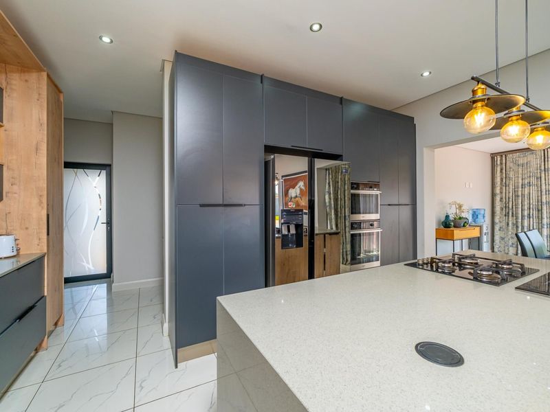 Modern kitchen featuring dark cabinetry, a large stone island with a gas cooktop, built-in double ovens, and sleek tiled flooring.