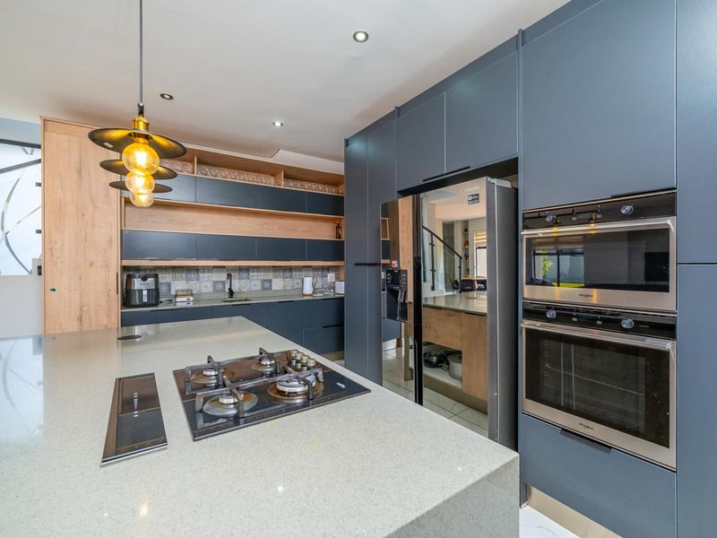 Modern kitchen featuring dark cabinetry, stone countertops, a central island with a gas hob, and integrated stainless steel appliances.