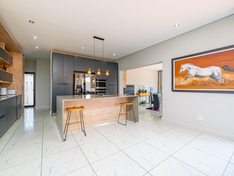 Modern open-plan kitchen featuring a central island, sleek dark cabinetry, built-in appliances, and high-quality marble-look floor tiles.