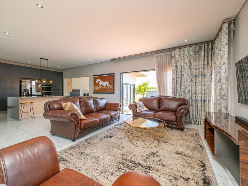 Spacious open-plan living area featuring modern tiled floors, recessed lighting, and a seamless transition to the kitchen and outdoor patio space.