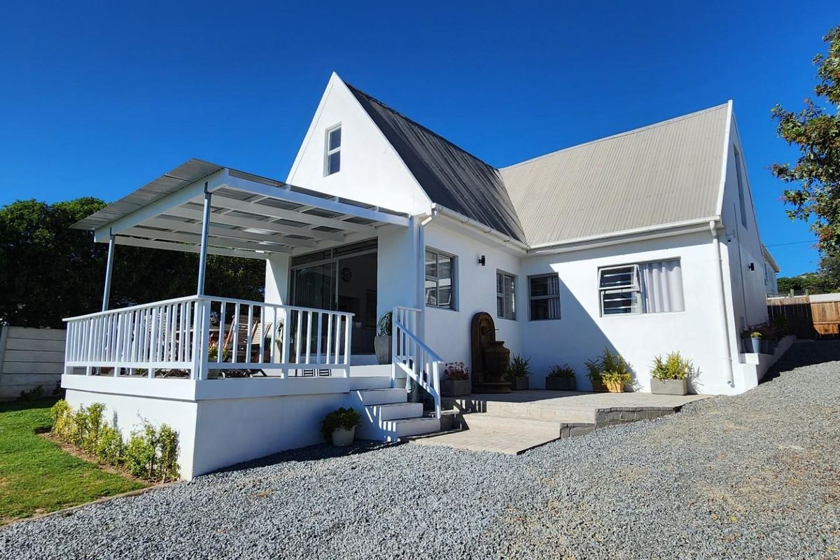 Rear view of the house featuring a white facade, a covered patio with white railings, a metal roof, and a gravel driveway.