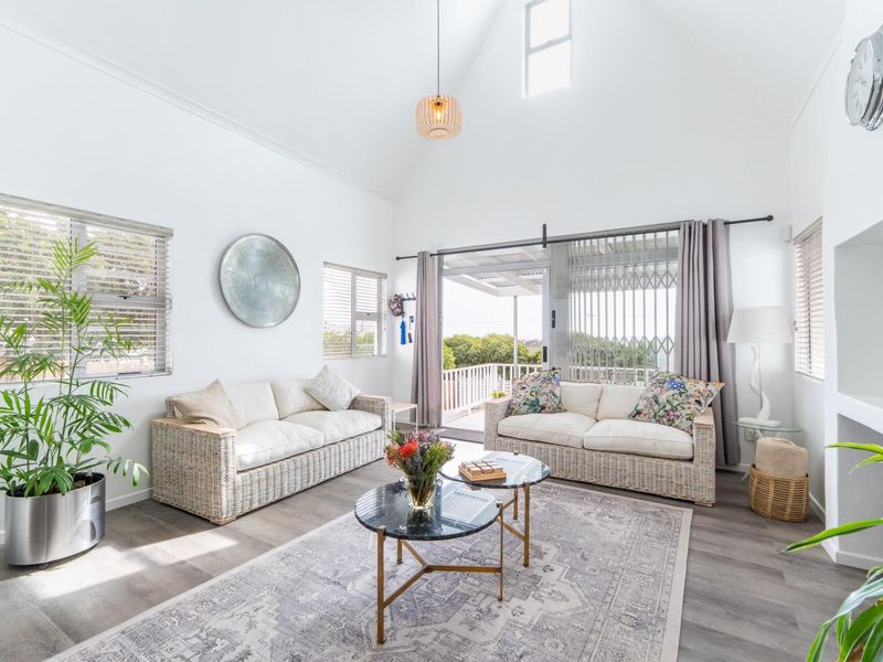 Bright and airy living room featuring a high vaulted ceiling, modern laminate flooring, and large sliding glass doors leading to an outdoor patio area.