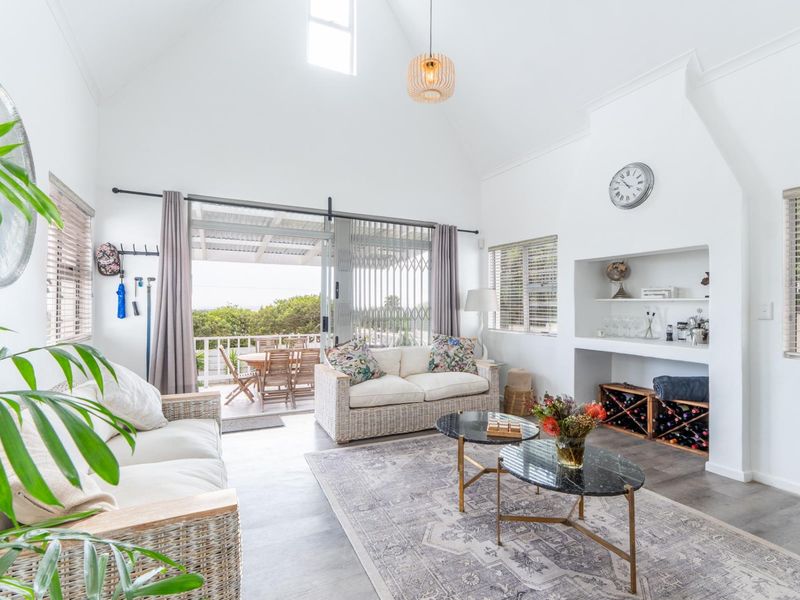 Bright and airy living room featuring a high vaulted ceiling, built-in shelving with integrated wine storage, and large sliding doors opening to a patio.