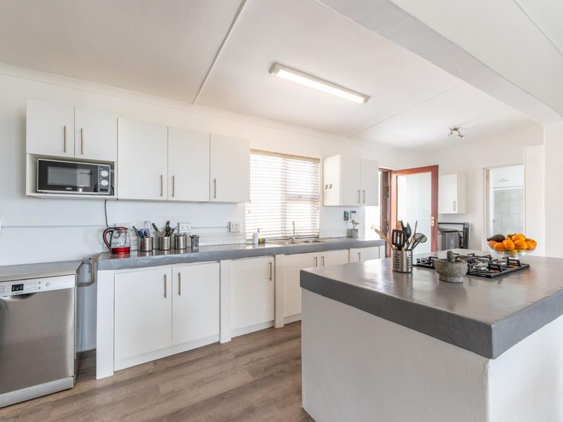 A bright, functional kitchen featuring white cabinetry, concrete countertops, a central island with a gas hob, and modern laminate flooring.