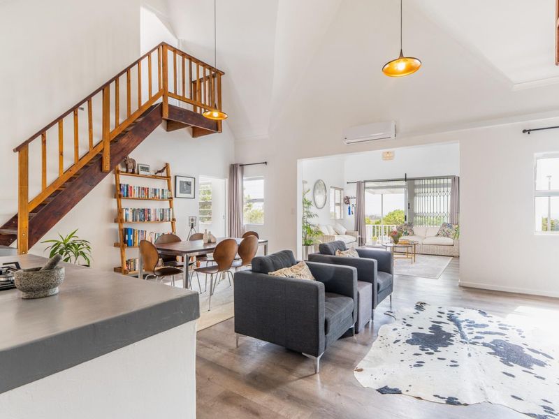 Spacious open-plan living area featuring vaulted ceilings, a wooden staircase, and seamless flow to an adjoining sunroom with laminate flooring throughout.