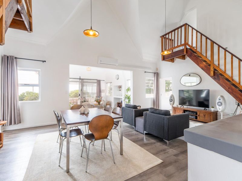 Spacious open-plan living and dining area featuring high vaulted ceilings, modern laminate flooring, and a prominent wooden staircase leading to an upper level.