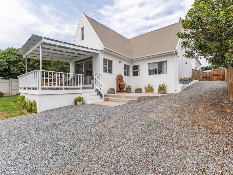 Rear view of the property featuring a covered patio, gravel driveway, and well-maintained white exterior walls with a metal roof.