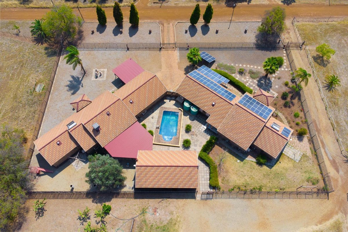 Aerial view of a farm property featuring a central swimming pool, courtyard, solar panel installation, and multiple roof structures within a fenced perimeter.