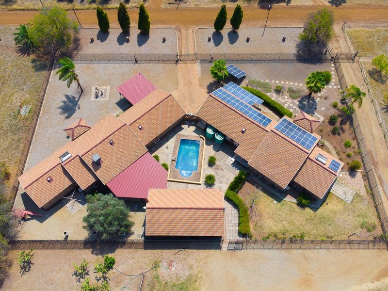Aerial view of a farm property featuring a central swimming pool, courtyard, solar panel installation, and multiple roof structures within a fenced perimeter.