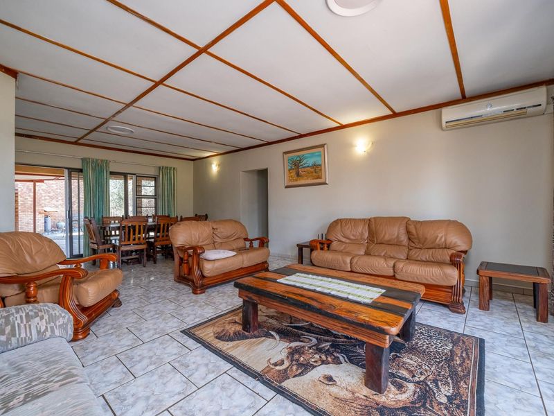 Spacious open-plan living and dining area featuring tiled flooring, an exposed beam ceiling, and direct access to the outdoor patio through sliding glass doors.