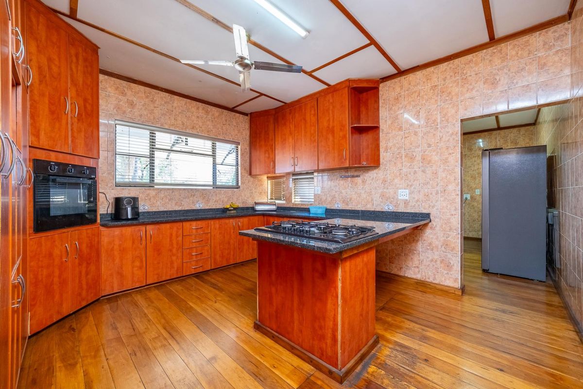 A functional kitchen featuring wooden cabinetry, granite countertops, a built-in oven, and a gas hob, with tiled walls and wooden flooring throughout.