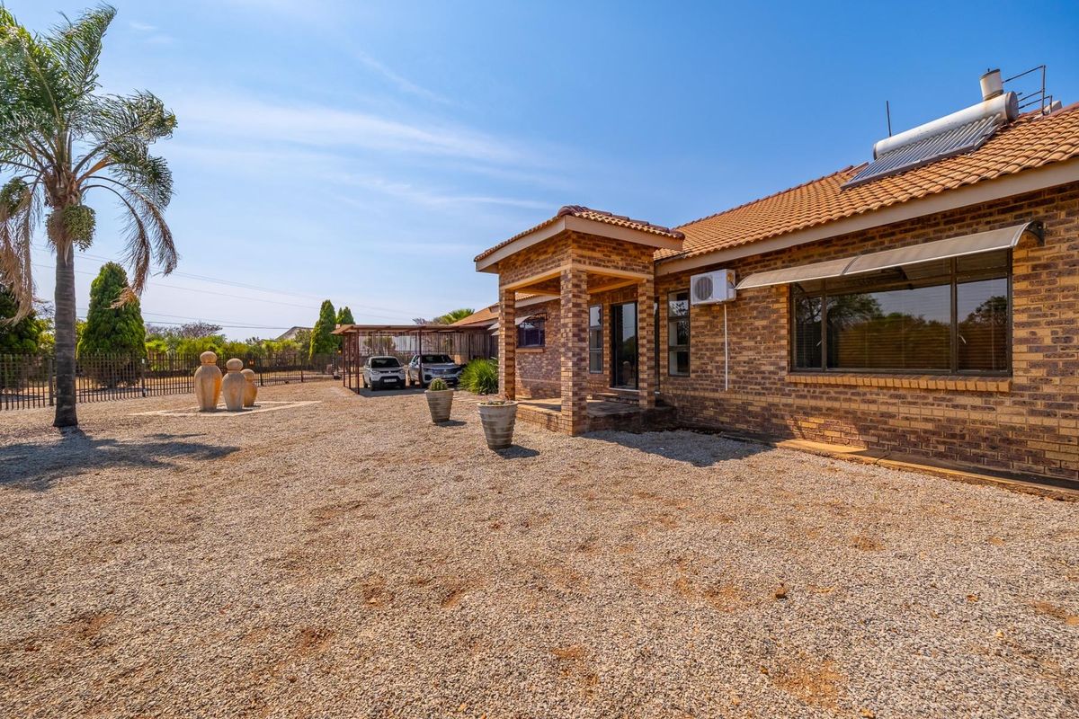 Rear view of a face brick farm house featuring a covered patio, solar water heater, and a spacious gravel yard with an attached carport.