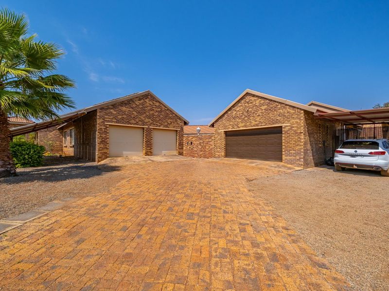 A well-maintained farm property featuring a paved driveway leading to a triple garage configuration and an attached carport.