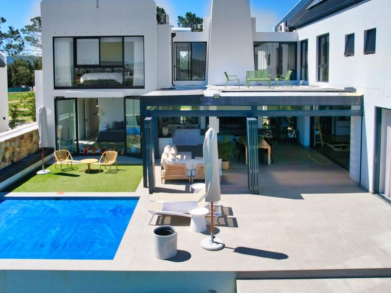 Rear exterior view featuring a modern swimming pool, covered patio area, stone-clad retaining wall, and an upper-level balcony with large glass sliding doors.