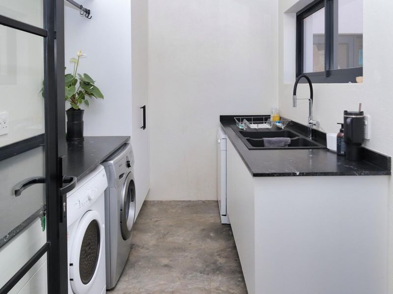 Modern laundry room featuring sleek black countertops, undermount sink, gooseneck faucet, and dedicated space for laundry appliances with polished concrete flooring.
