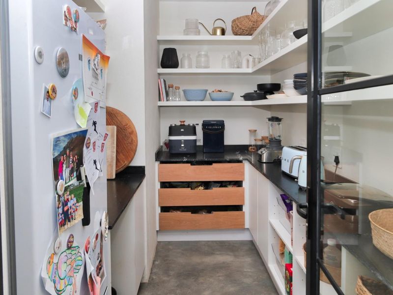 A functional scullery featuring stone countertops, open shelving, and wooden storage drawers, providing additional prep and storage space adjacent to the main kitchen.