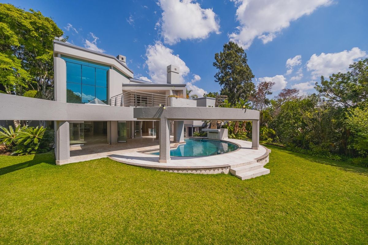 Rear view of a modern architectural home featuring a swimming pool, covered patio area, expansive glass windows, and a well-maintained garden.