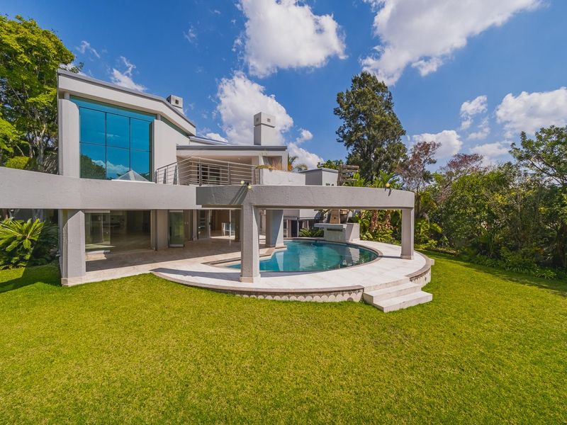 Rear view of a modern architectural home featuring a swimming pool, covered patio area, expansive glass windows, and a well-maintained garden.