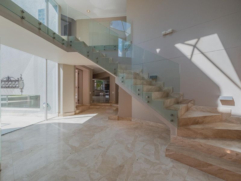 Spacious double-volume entrance hall featuring a striking floating marble staircase with a modern glass balustrade and polished marble flooring.