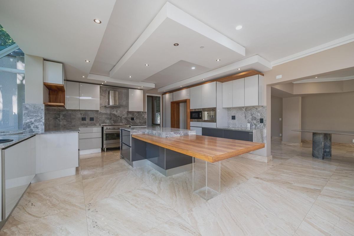Modern kitchen featuring high-gloss cabinetry, stone countertops, a large central island with a wooden breakfast bar, and integrated appliances.