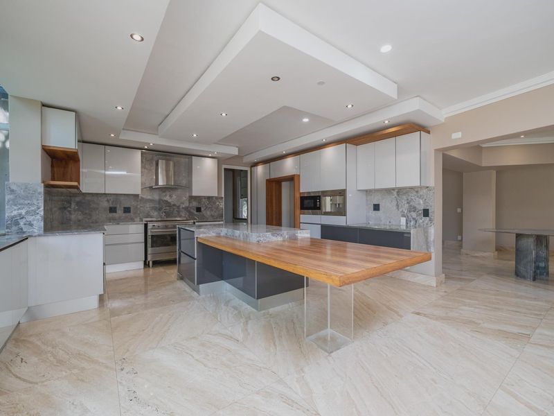 Modern kitchen featuring high-gloss cabinetry, stone countertops, a large central island with a wooden breakfast bar, and integrated appliances.
