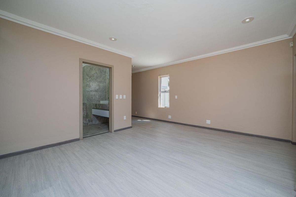 A spacious, empty bedroom featuring light-toned laminate flooring, neutral walls, crown molding, and recessed lighting, with an adjoining en-suite bathroom.