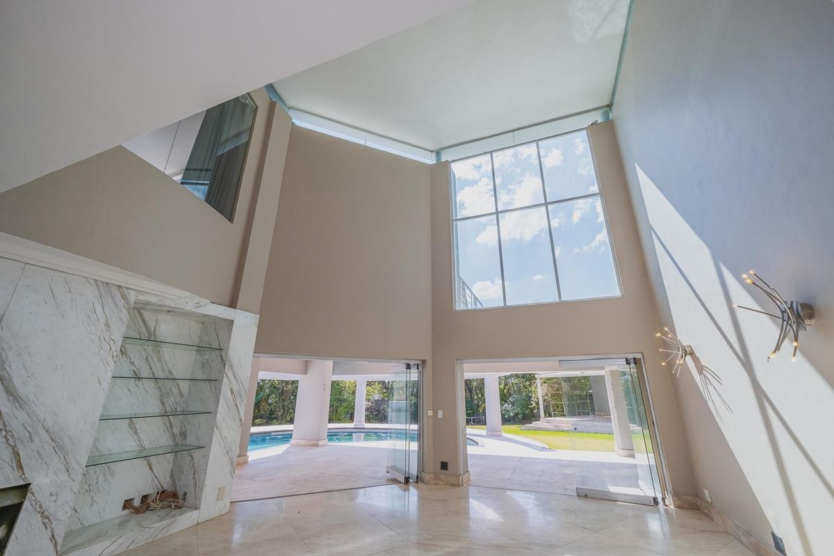 Spacious double-volume living area featuring marble flooring, a built-in marble fireplace, and expansive glass doors opening directly to the pool and garden area.