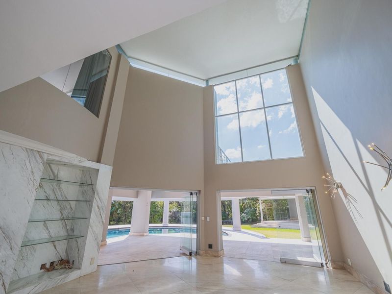 Spacious double-volume living area featuring marble flooring, a built-in marble fireplace, and expansive glass doors opening directly to the pool and garden area.