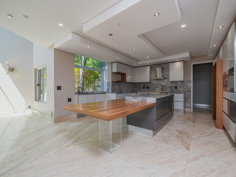 Modern kitchen featuring a large island with a wooden breakfast bar, stone countertops, high-end cabinetry, and marble tile flooring in an open-plan layout.