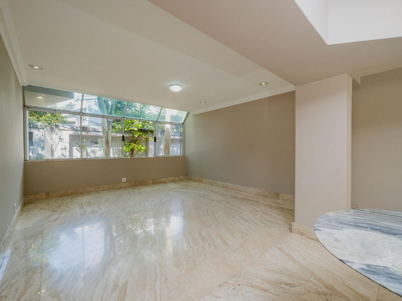 A bright and spacious living area featuring polished marble flooring, recessed lighting, and a large window providing natural light and garden views.