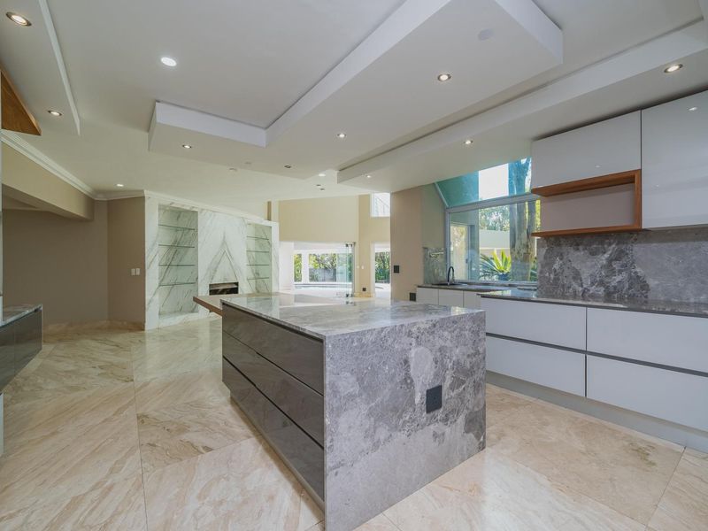 Spacious open-plan kitchen and living area featuring high-end marble finishes, a central island, built-in appliances, and modern recessed ceiling lighting.