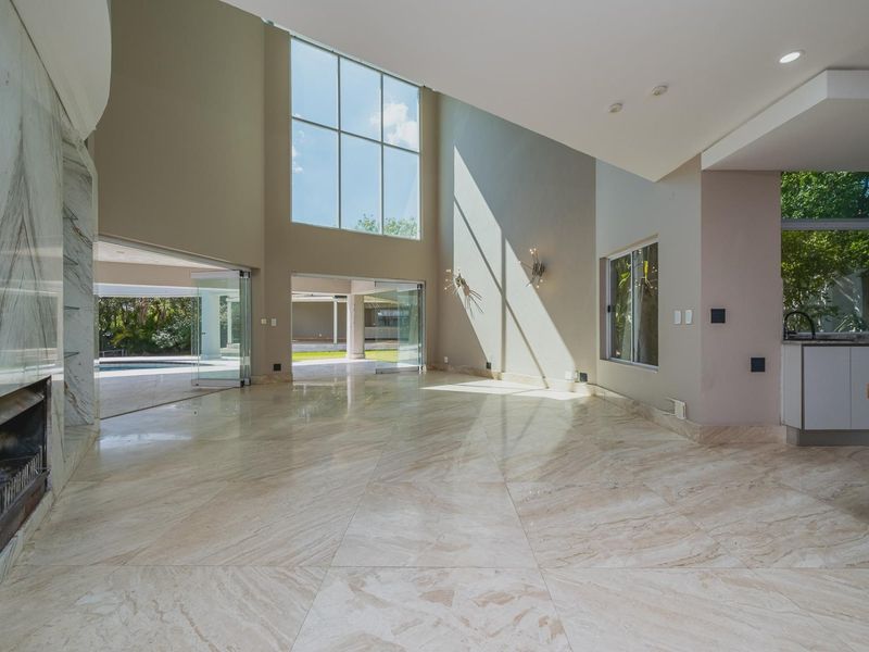 Spacious open-plan living area featuring high double-volume ceilings, marble flooring, a feature fireplace, and large stacking doors opening to the outdoor pool area.