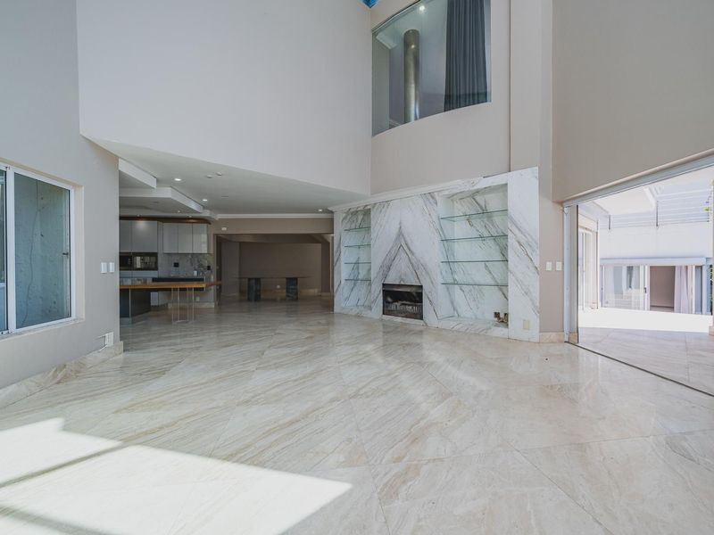 Spacious open-plan living area featuring high double-volume ceilings, polished marble flooring, and a striking marble-clad fireplace with integrated glass shelving.