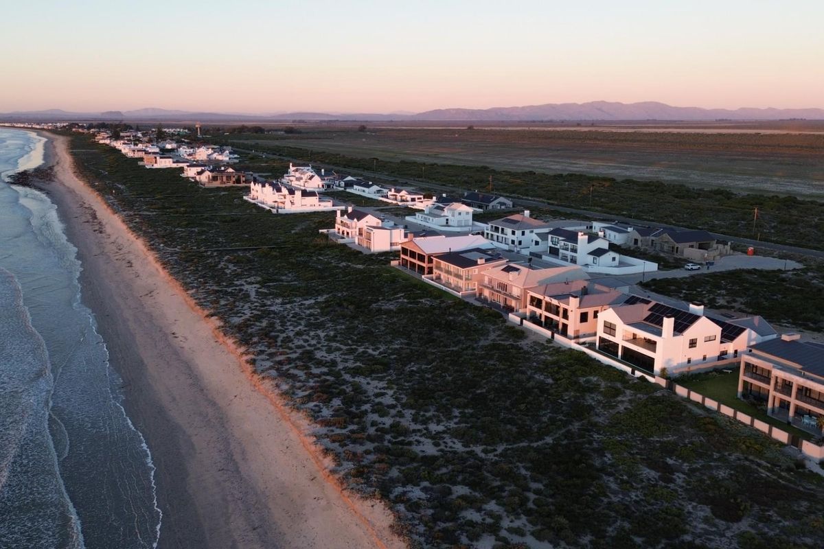 An aerial view of a coastal residential estate situated along the beachfront, showcasing the surrounding landscape and proximity to the ocean.