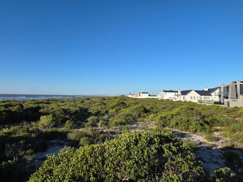 A scenic view of the coastal landscape featuring native vegetation, sandy terrain, and nearby residential properties along the shoreline.