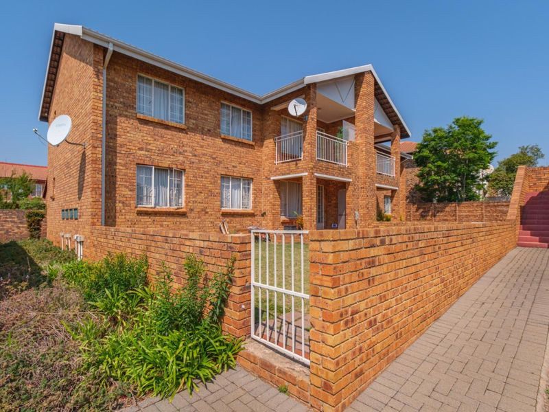 A view of the front elevation of a face brick apartment building featuring a paved walkway, private garden area, and balcony access.