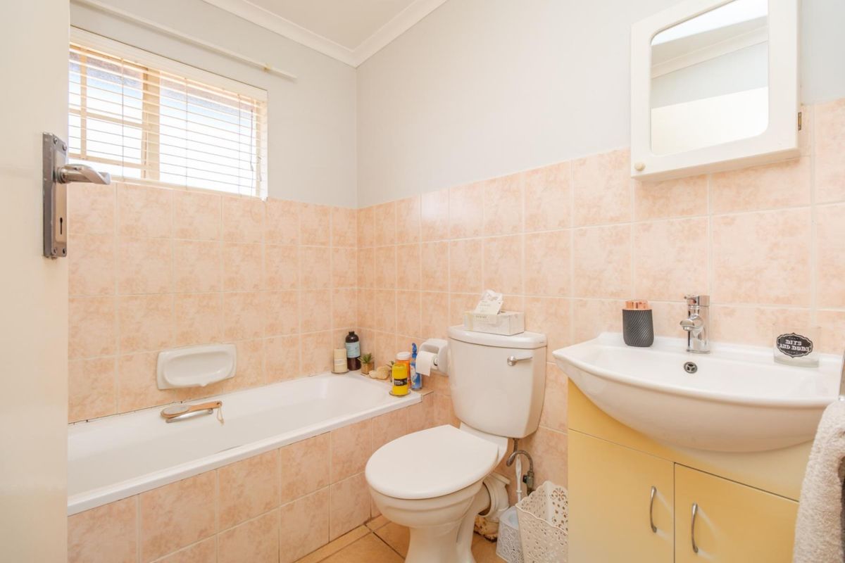 A functional bathroom featuring a bathtub, toilet, and vanity basin with cabinet storage, finished with neutral wall and floor tiling.