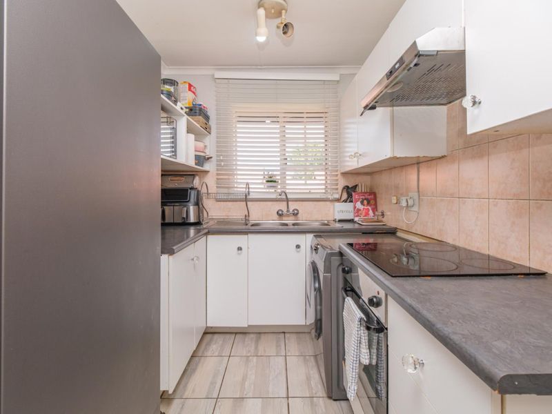 Compact kitchen featuring white cabinetry, dark laminate countertops, integrated electric hob, oven, extractor fan, and tiled backsplash with neutral floor tiles.
