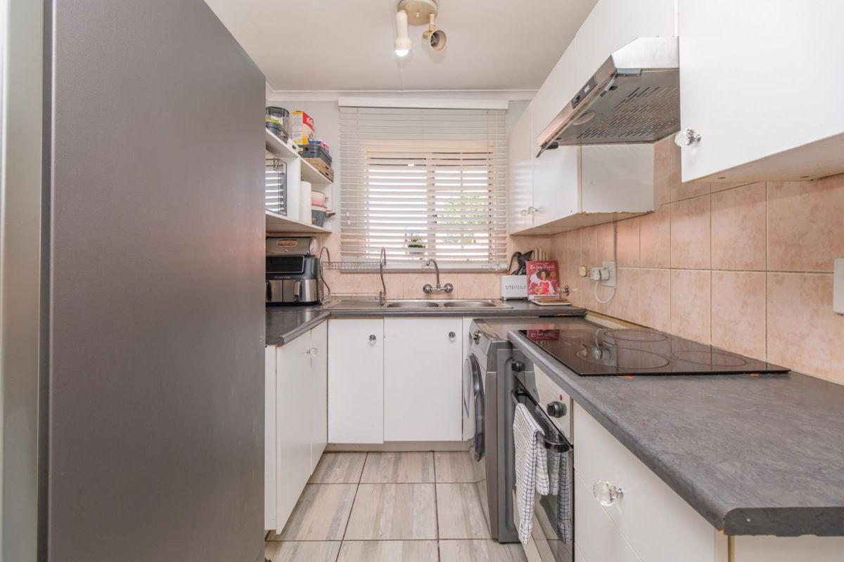 Compact kitchen featuring white cabinetry, dark laminate countertops, integrated electric hob, oven, extractor fan, and tiled backsplash with neutral floor tiles.