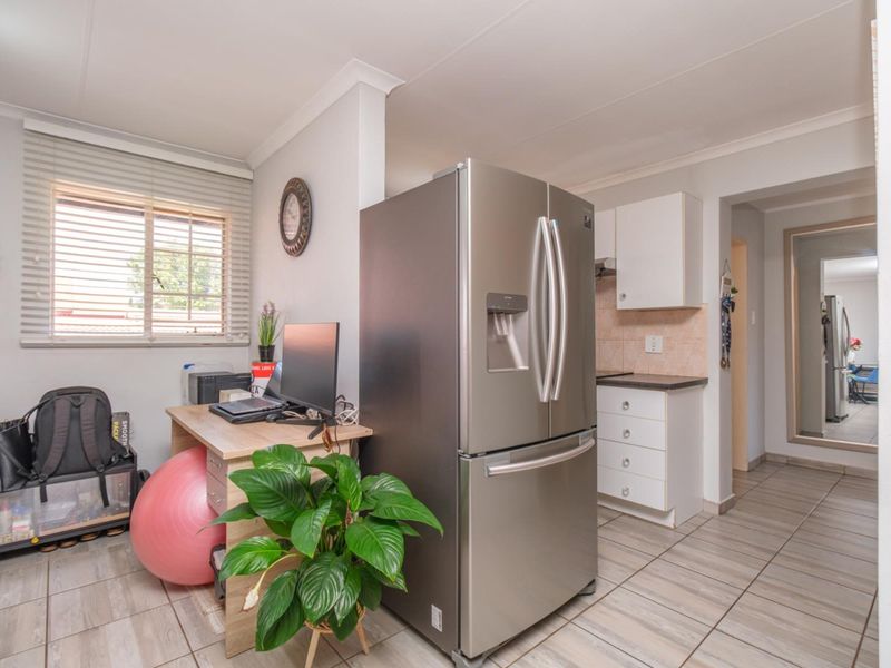 Open-plan living area featuring tiled flooring, a functional kitchen with built-in cabinetry, and natural light through venetian blinds.