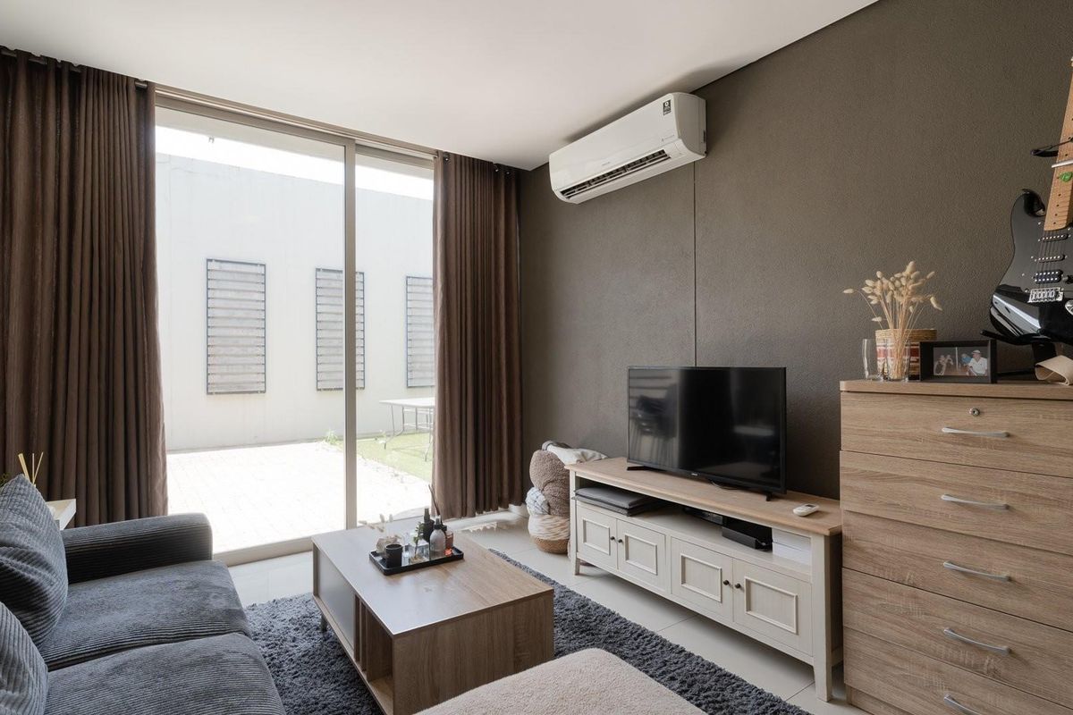 A well-maintained living room featuring tiled flooring, a wall-mounted split-system air conditioner, and large sliding glass doors providing access to an outdoor patio area.