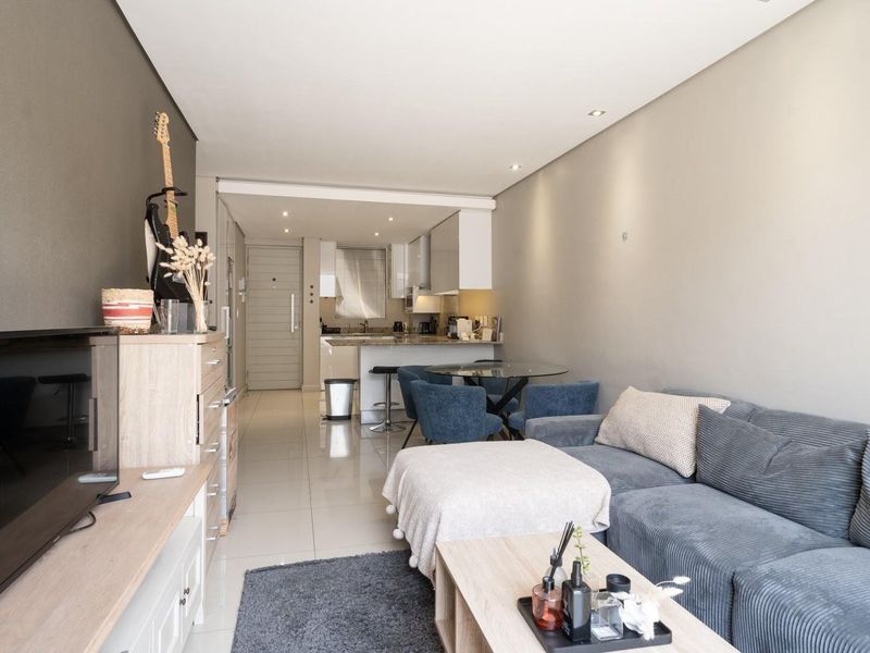 An open-plan living and kitchen area featuring modern tiled flooring, recessed lighting, and a functional kitchen layout with built-in cabinetry.