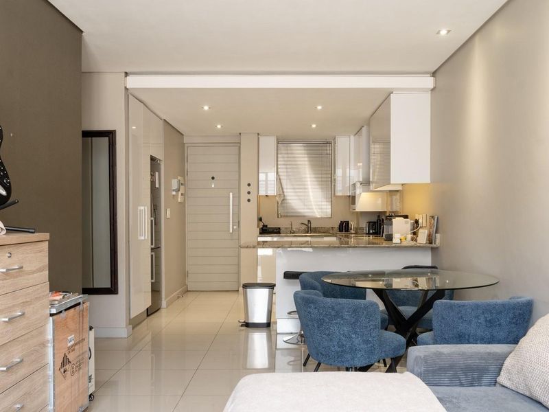 Modern open-plan apartment featuring a sleek kitchen with granite countertops, tiled flooring, and recessed lighting, seamlessly flowing into the living and dining area.