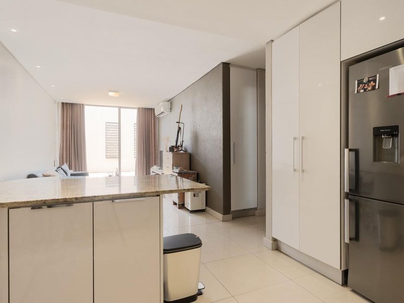 Modern open-plan living area featuring a sleek kitchen with granite countertops, gloss cabinetry, and tiled flooring, seamlessly flowing into the living space.