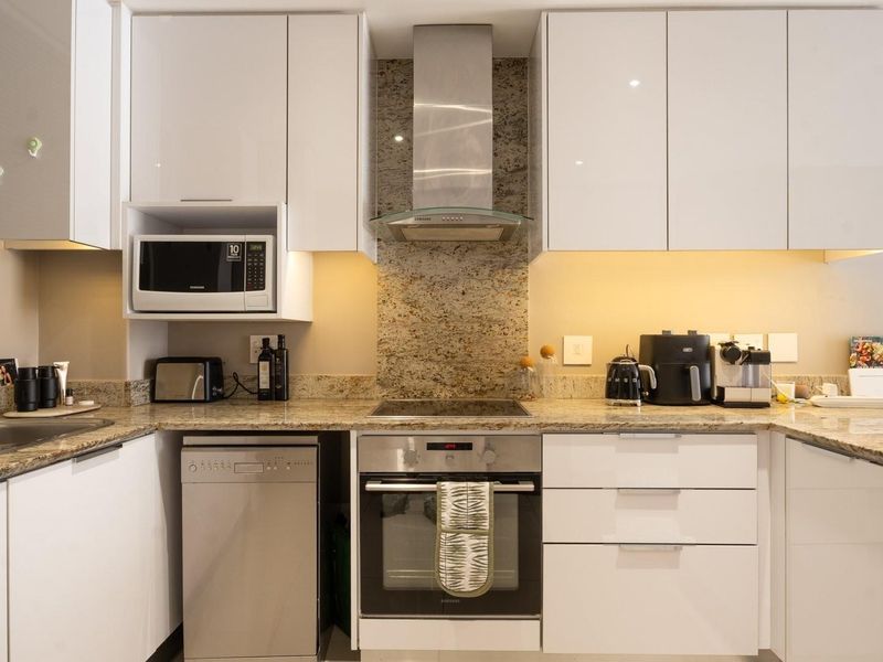 Modern kitchen featuring high-gloss white cabinetry, granite countertops, integrated stainless steel appliances, and under-cabinet lighting for a clean, functional workspace.