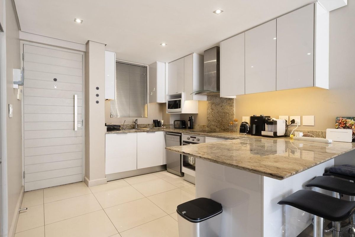 Modern kitchen featuring sleek white cabinetry, granite countertops, integrated appliances, and recessed lighting, creating a clean and functional culinary space.